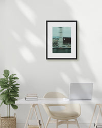 Framed artwork on a wall above a desk with a plant and laptop.