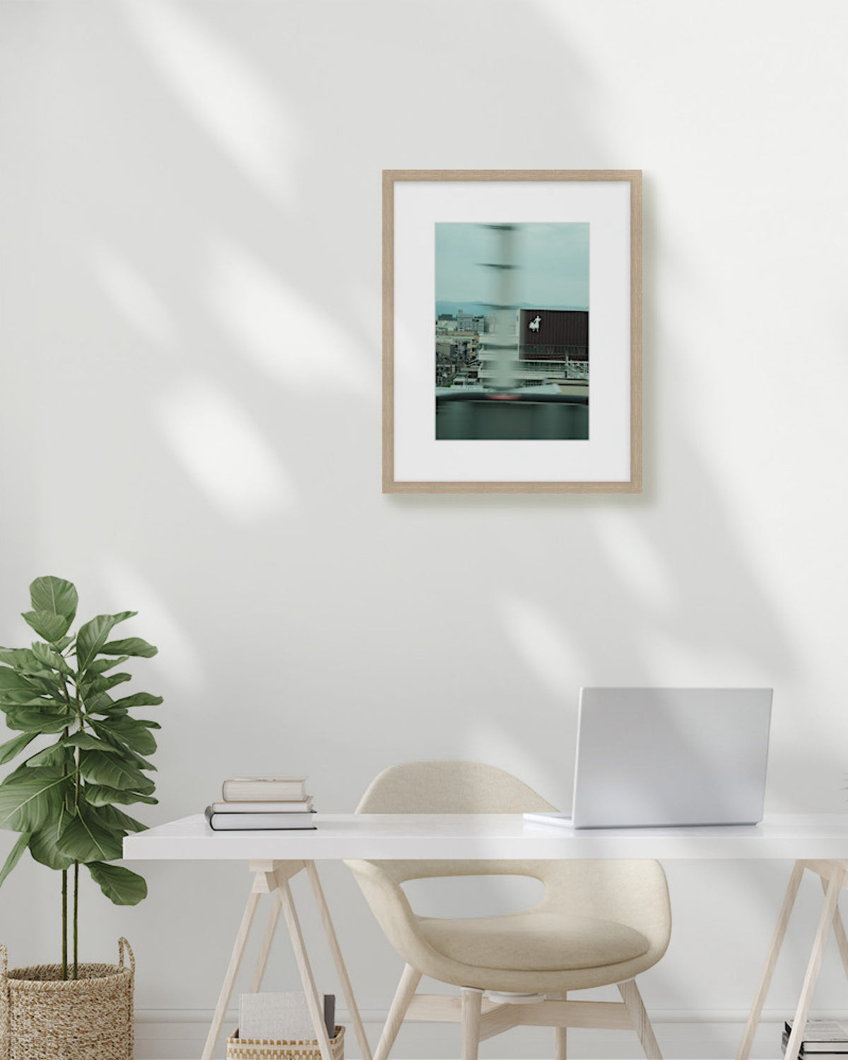 Framed artwork on a wall above a desk with a plant and laptop.