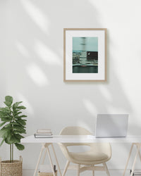 Framed artwork on a wall above a desk with a plant and laptop.