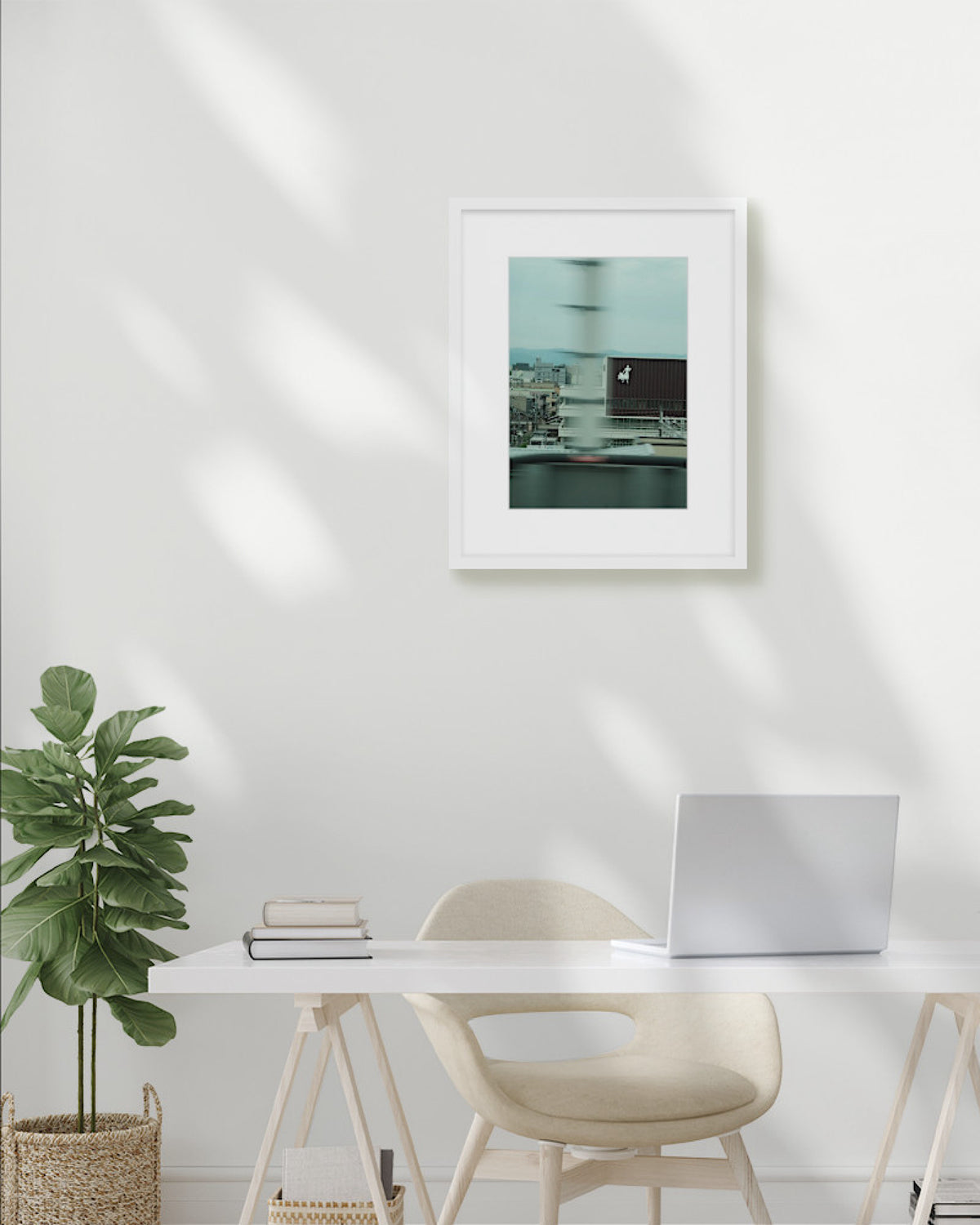 Modern office setup with a desk, chair, plant, and framed picture on a white wall.