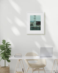 Modern office setup with a desk, chair, plant, and framed picture on a white wall.