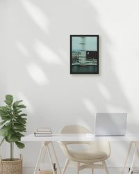 Modern office setup with a desk, chair, plant, and framed picture on a white wall.