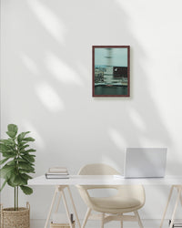 Modern home office with a desk, chair, plant, and framed picture on a white wall.