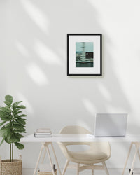 Modern home office with a desk, chair, plant, and framed picture on a white wall.