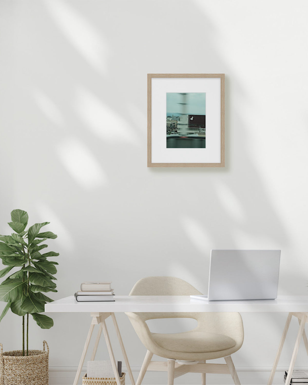 Modern home office with a desk, chair, plant, and framed picture on a white wall.
