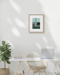 Modern home office with a desk, chair, plant, and framed picture on a white wall.