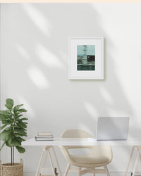 Modern office setup with a desk, chair, plant, and framed picture on a white wall.