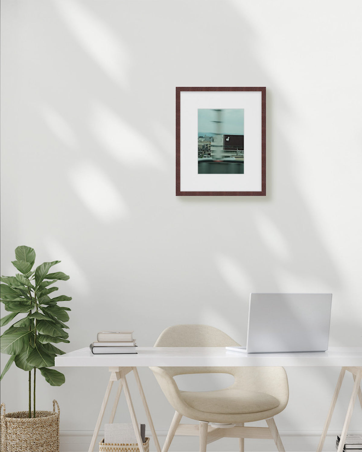 Modern office setup with a desk, chair, plant, and framed picture on a white wall.