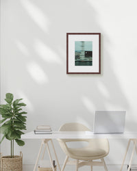 Modern office setup with a desk, chair, plant, and framed picture on a white wall.