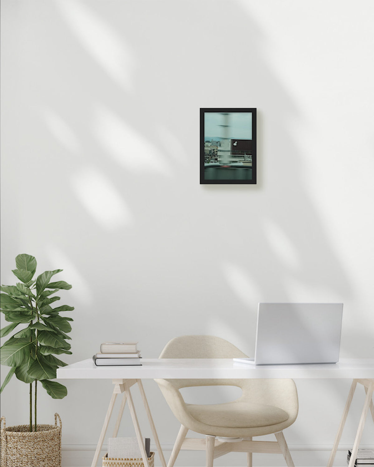 Modern home office with a desk, chair, plant, and framed picture on a white wall.
