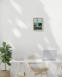Modern home office with a desk, chair, plant, and framed picture on a white wall.