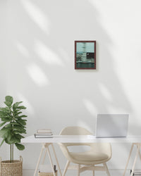 Modern office setup with a desk, chair, plant, and framed picture on a white wall.