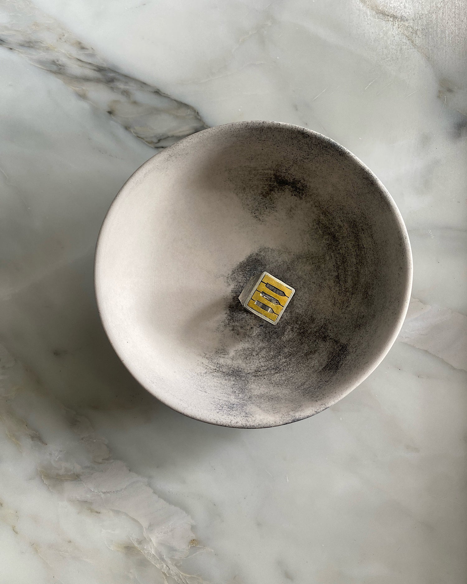 a brass faced ring with silver border and band by Johnny Ramli sits in a bowl. Available at The Pared Store