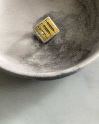 A silver and brass faced ring with three holes in the face sits in a bowl