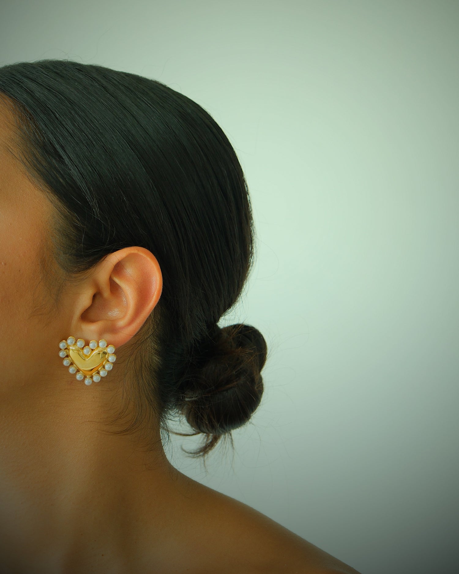 Model wears gold heart and pearl earrings