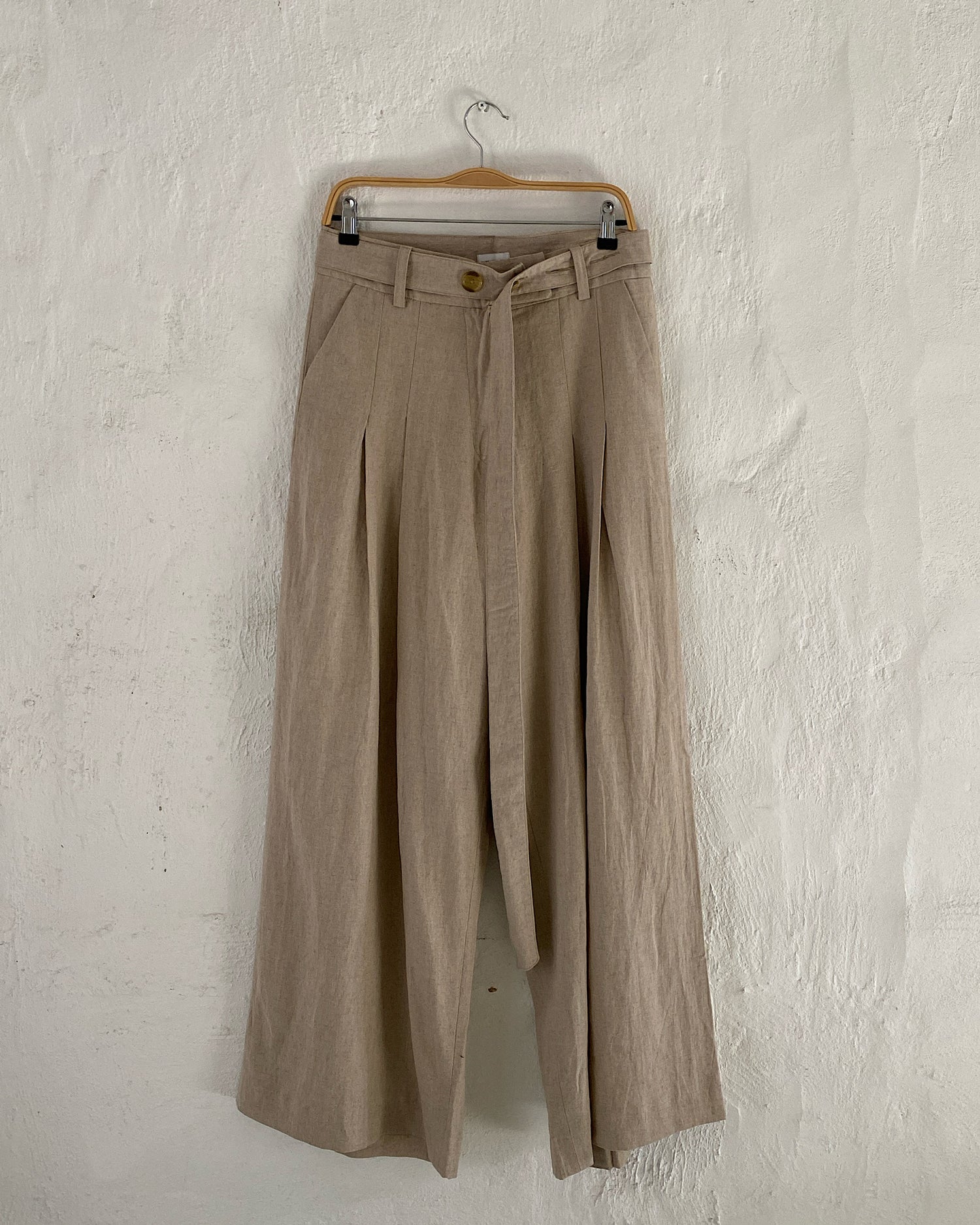 natural wide leg trousers sit on a hanger against a wall