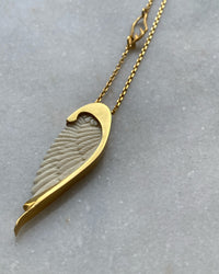 Long gold chain with a handcarved bone Wine pendant by Johnny Ramli sits on Marble