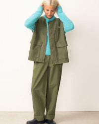 Person wearing a green vest and pants set with a blue sweater against a white background