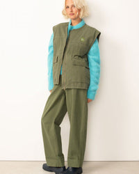 Person wearing a green vest and pants with a blue sweater against a white background