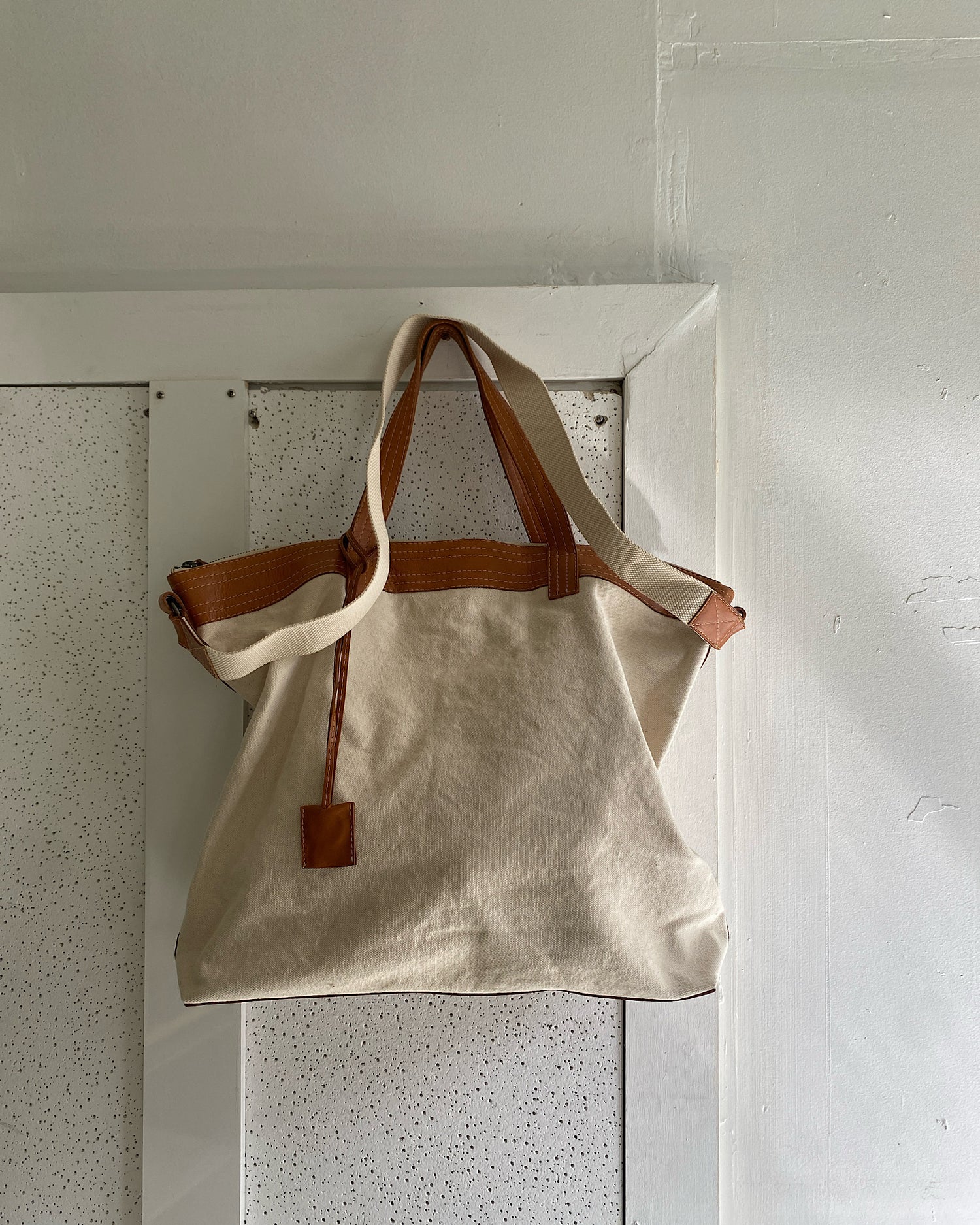 Natural canvas and Tan leather overnight bag with straps on a wall