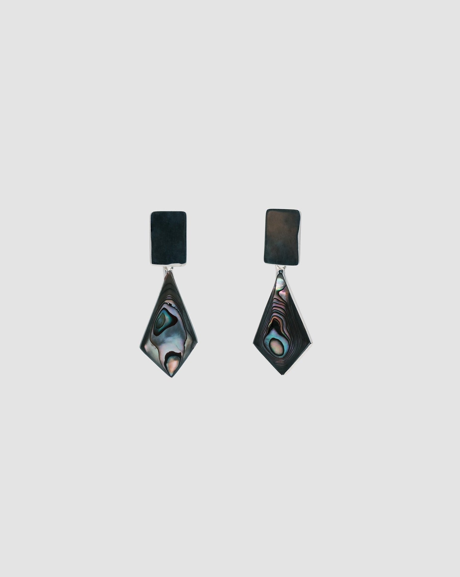 Earrings on a grey background that feature silver rectangle studs with abalone kite shaped charms
