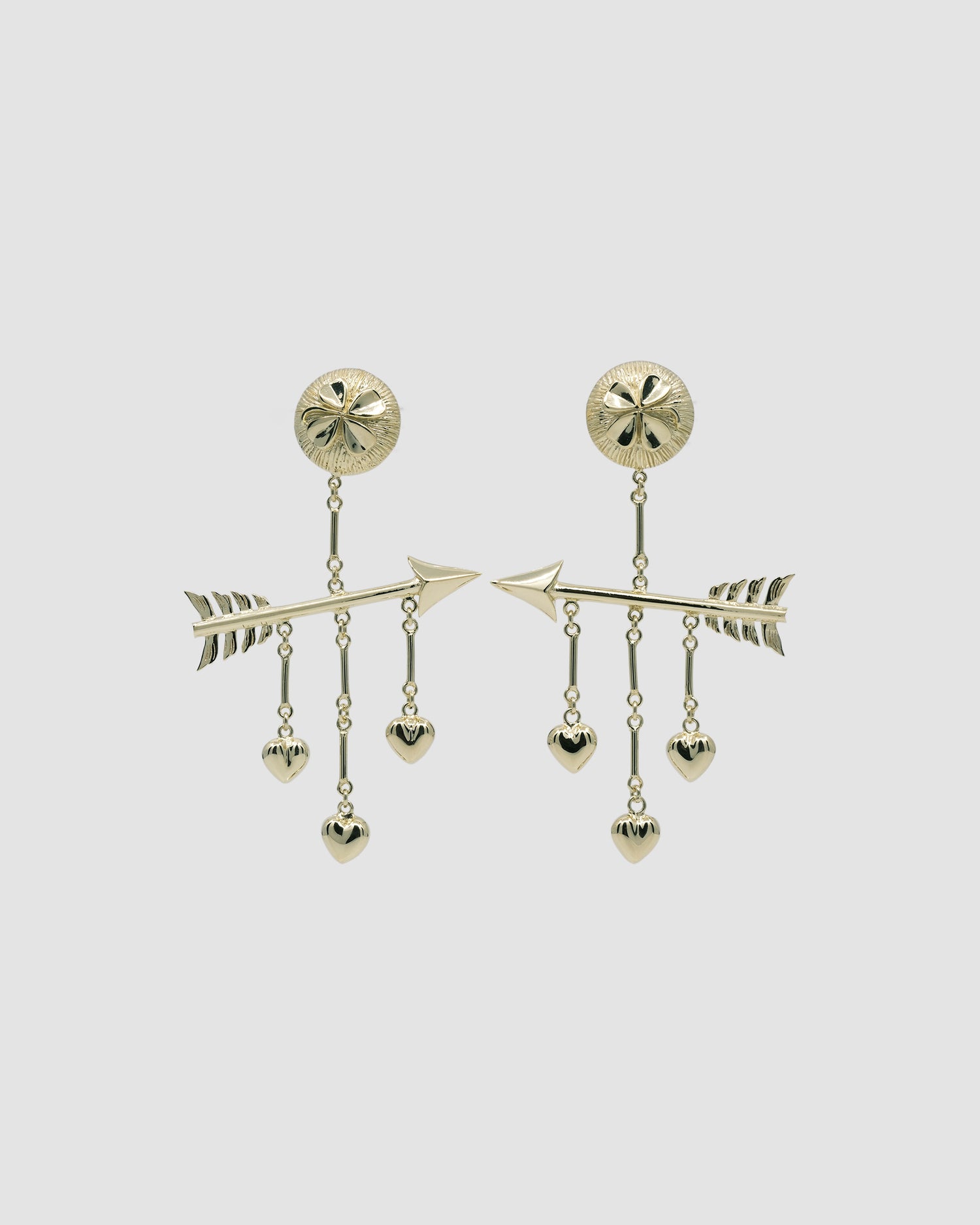 gold earrings featuring clover, hearts and arrow against a grey background