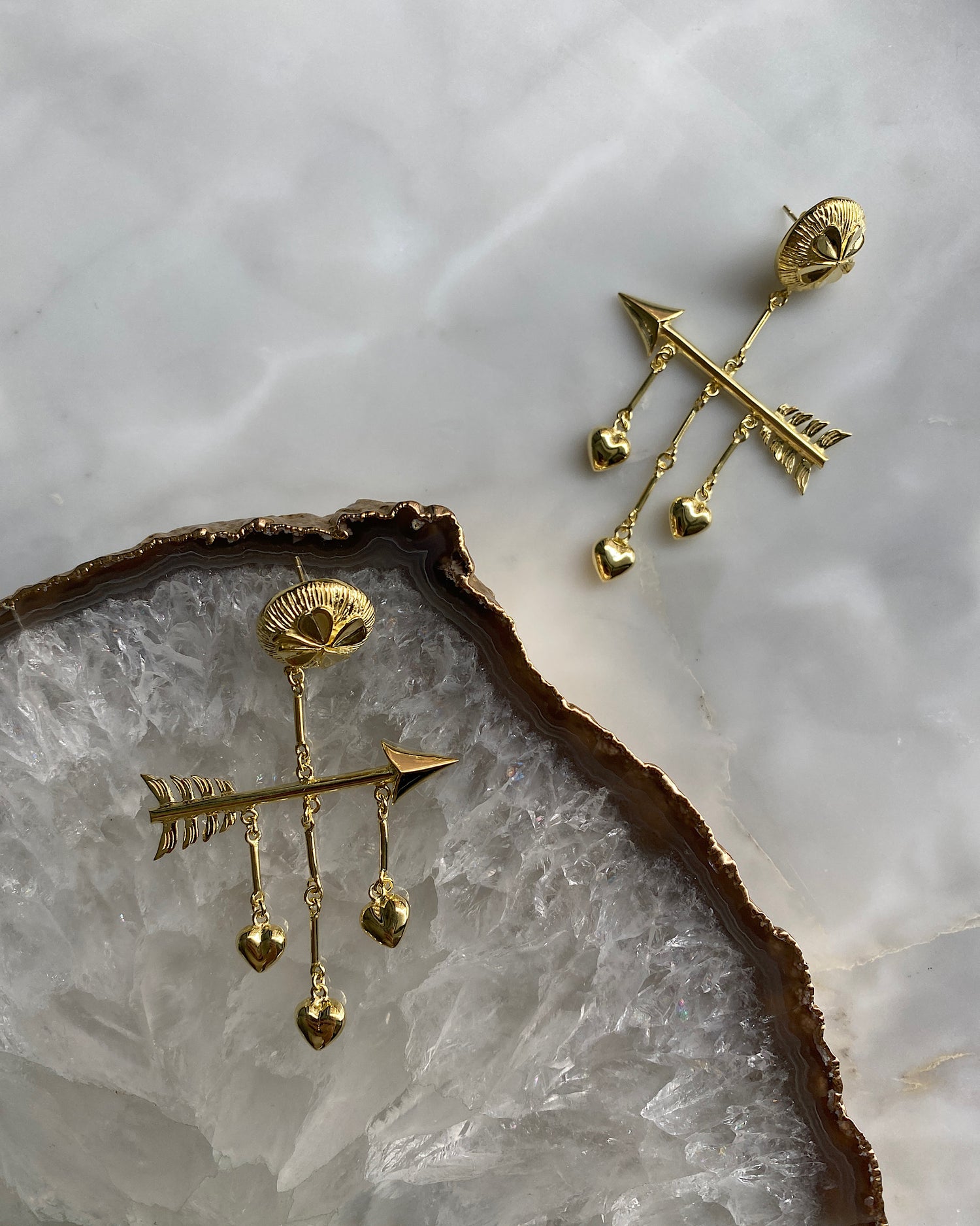 ormate gold earrings featuring hearts & arrows sit on a crystal platter