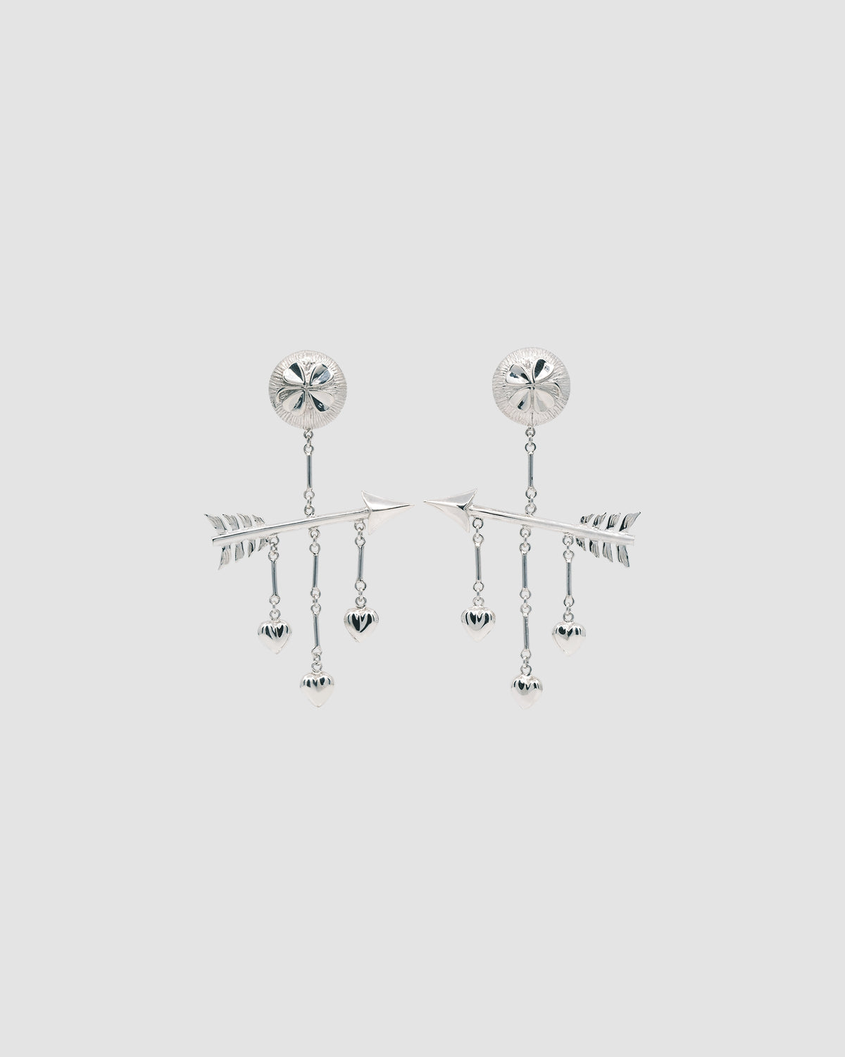 a pair of earrings featuring arrow, hearts and four leaf clover against a grey background