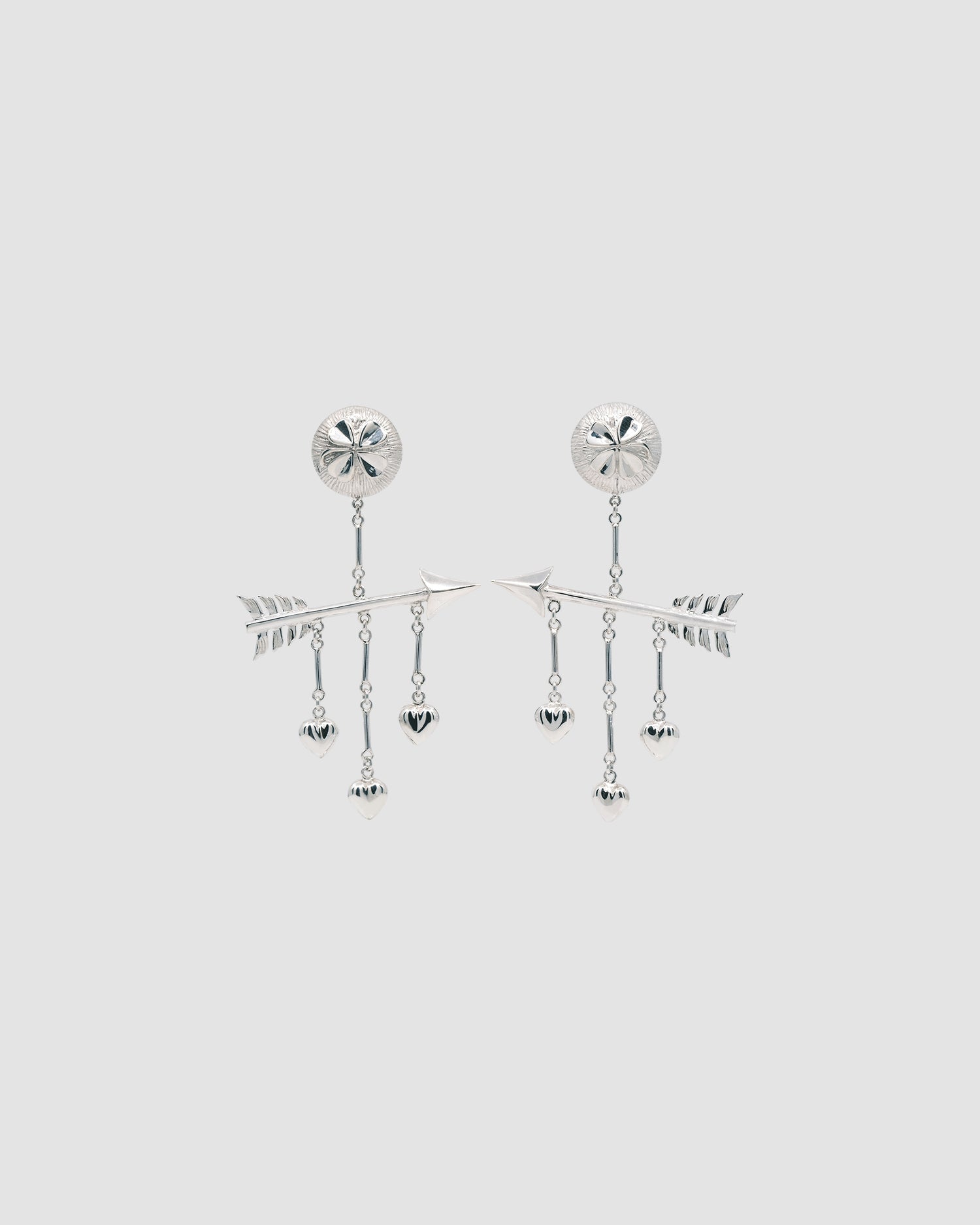 a pair of earrings featuring arrow, hearts and four leaf clover against a grey background