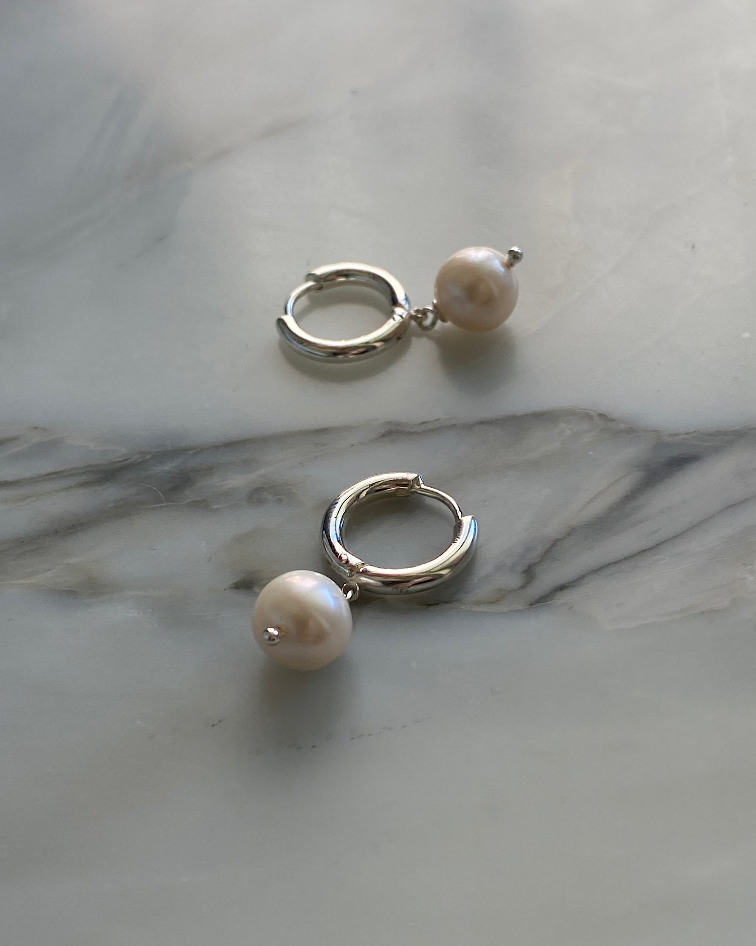 Small round pearls hang off a huggie style silver earring. Pictured on a marble background. Pearl Earrings Australia