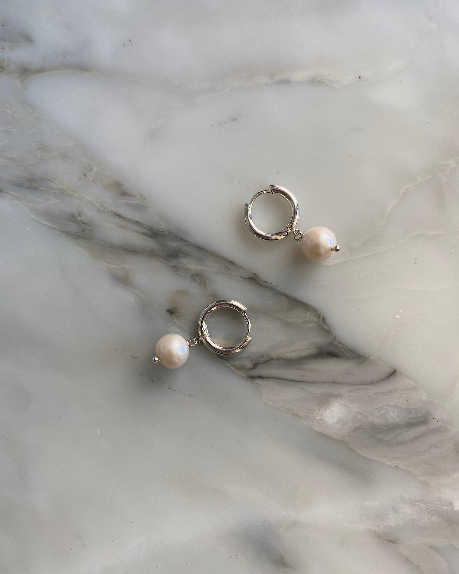 Pearl Earrings Sydney - mall round pearls hang off a huggie style silver earring. Pictured on a marble background