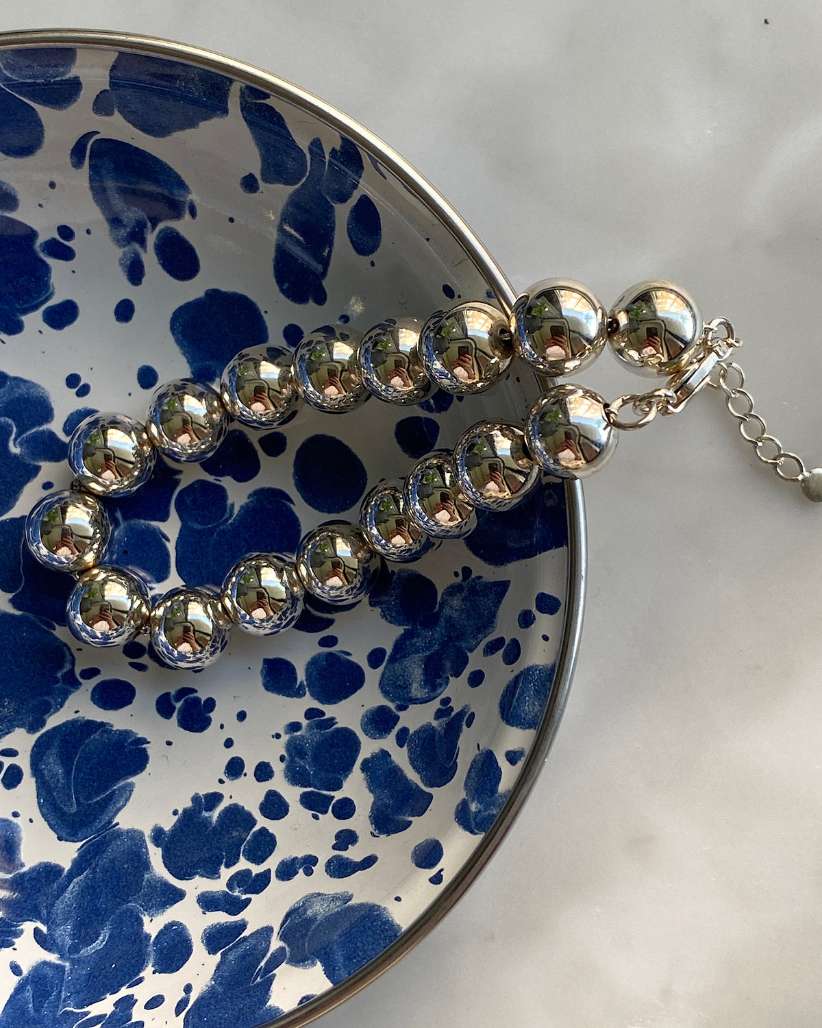 a closeup of a silver ball bracelet in a mottled blue bowl