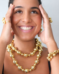 a model wears gold ball necklaces, bracelets, rings and earrings