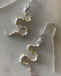 closeup of silver snake thread earrings with gold bands