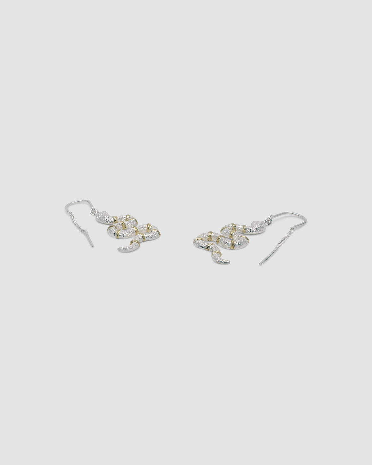 silver snake thread earrings with gold stripe details lie on a grey background