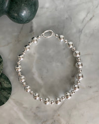 Large and mid size silver ball statement necklace with a simple clasp sits on marble