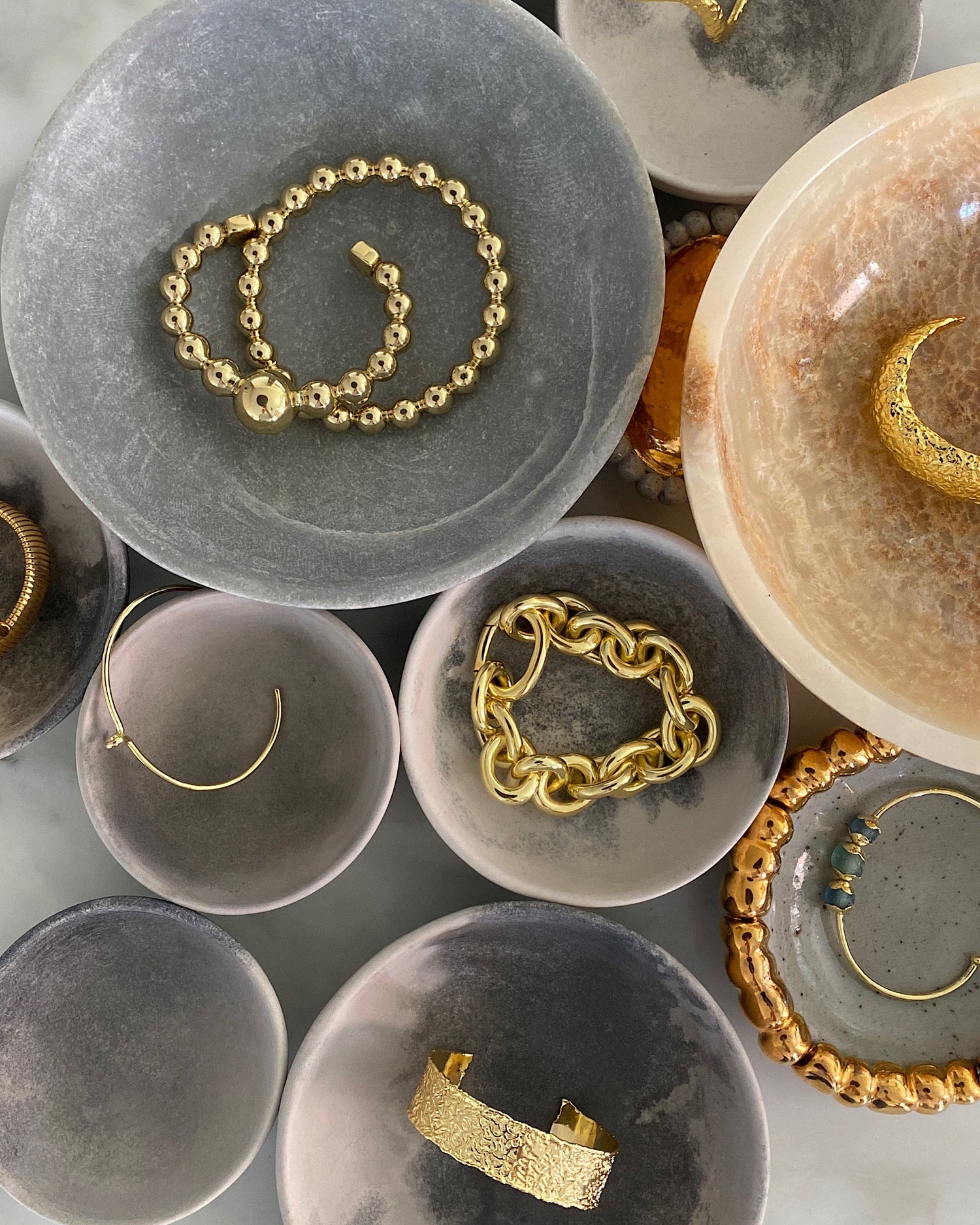 a group of stones bowls in various sizes filled with an assortment of gold bangles and bracelets