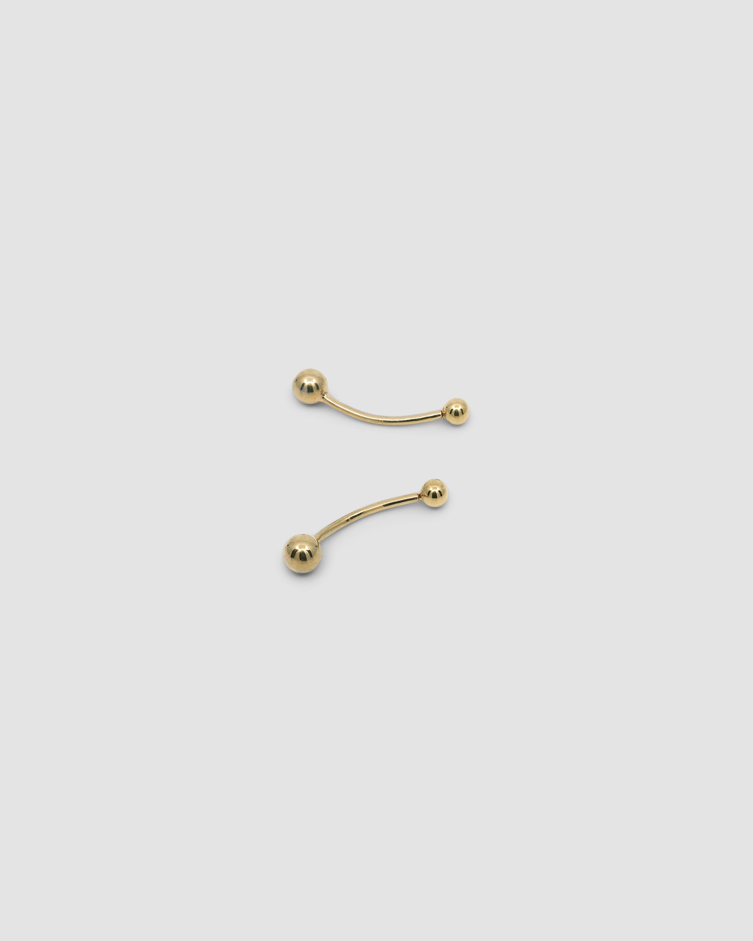 gold bar earrings with a ball at each end on a grey background