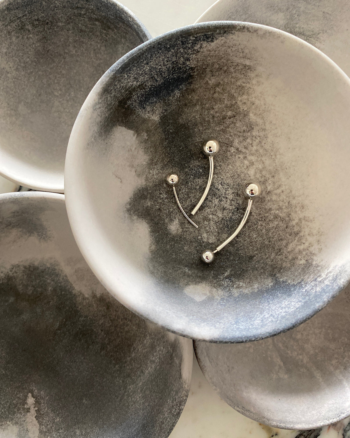 a pair of silver simple ball end earrings it in a bowl - one open and one closed