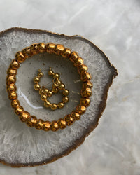 brass hoop earrings consisting if numberous balls joined together to form a hoop sit on a marble background in a gold rimmed bowl