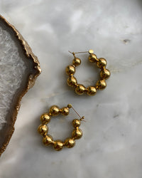 brass hoop earrings consisting if numberous balls joined together to form a hoop sit on a marble background