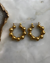 brass hoop earrings consisting if numerous balls joined together to form a hoop sit on a marble background