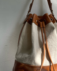 A tan trim canvas bucket bag sits on a wall The Pared Store