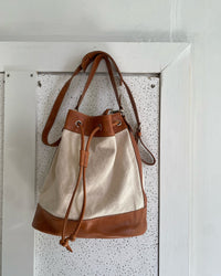 A tan trim canvas bucket bag sits on a wall The Pared Store