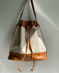 A tan trim canvas bucket bag sits on a wall The Pared Store