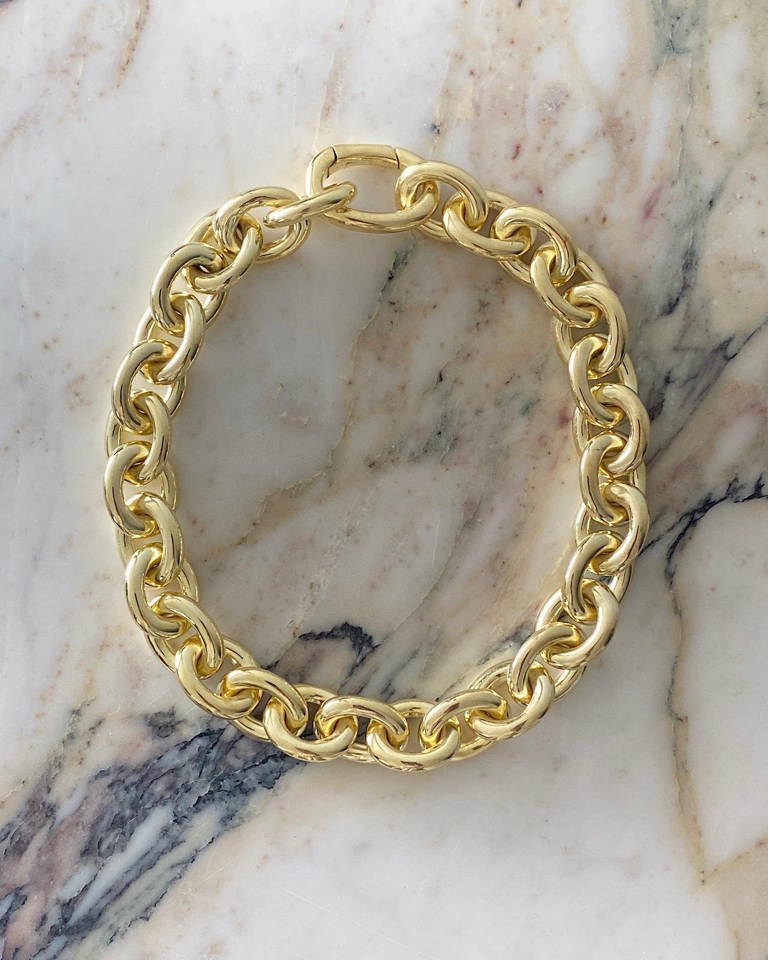 A chunky gold chain necklace sits on a marble background