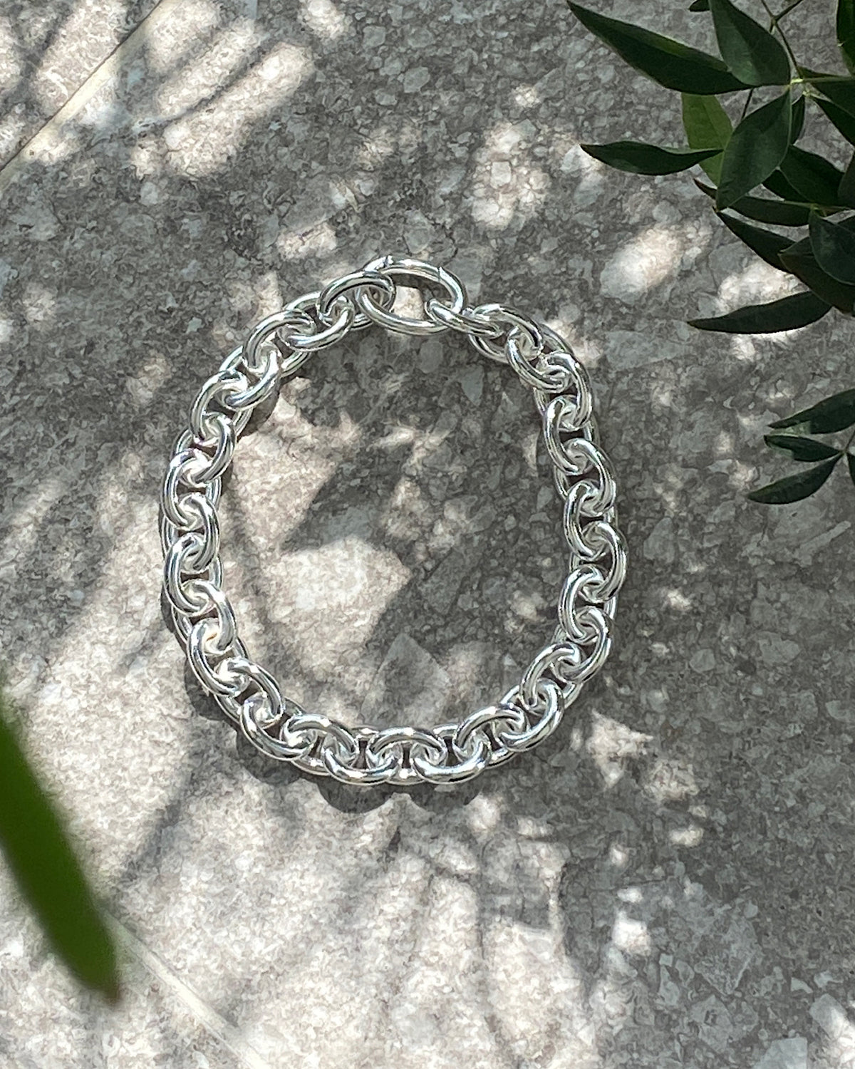 A chunky silver chain necklace sits on a concrete