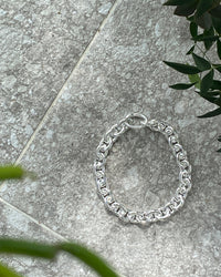 A chunky silver chain necklace sits on a concrete