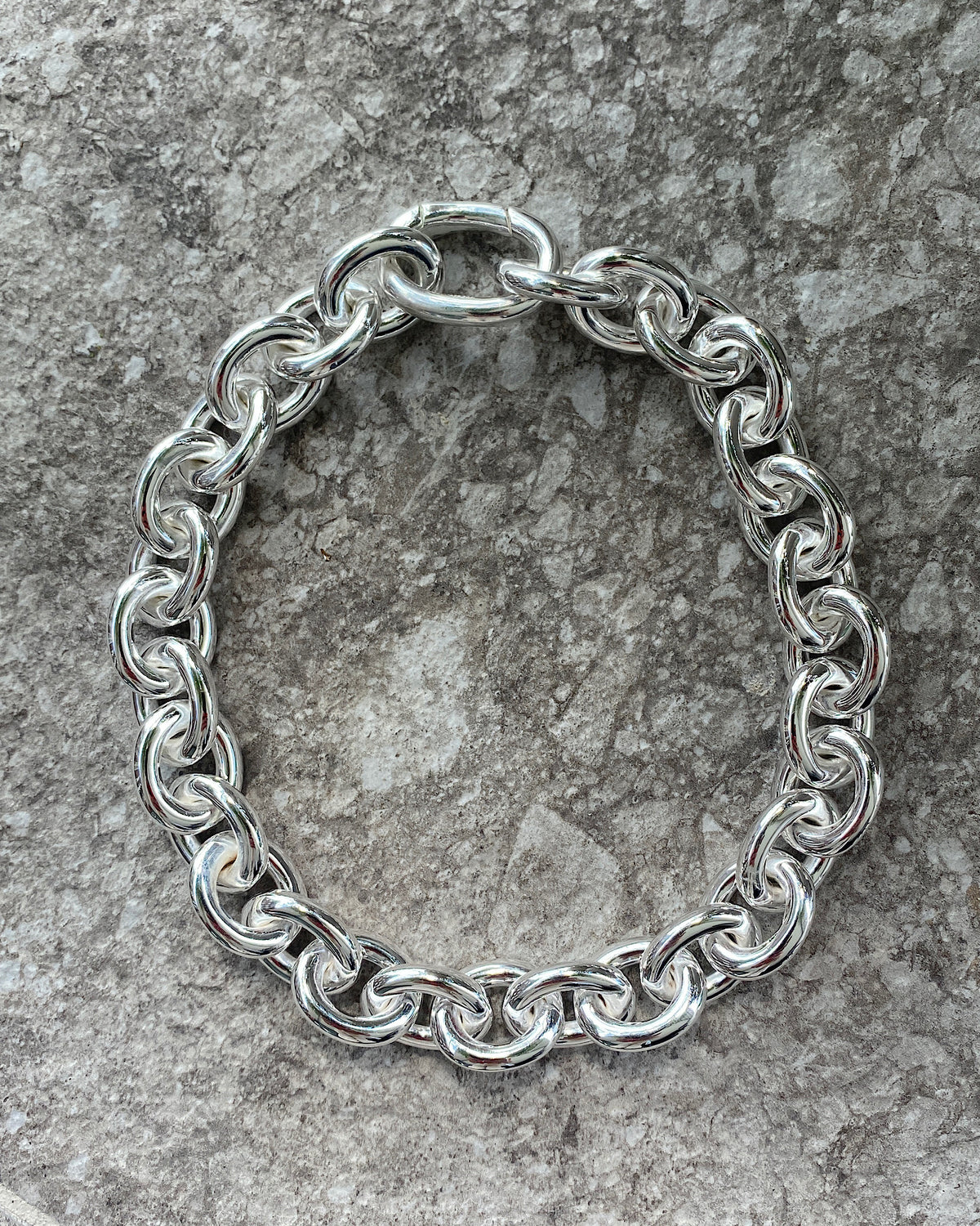 A chunky silver chain necklace sits on a concrete