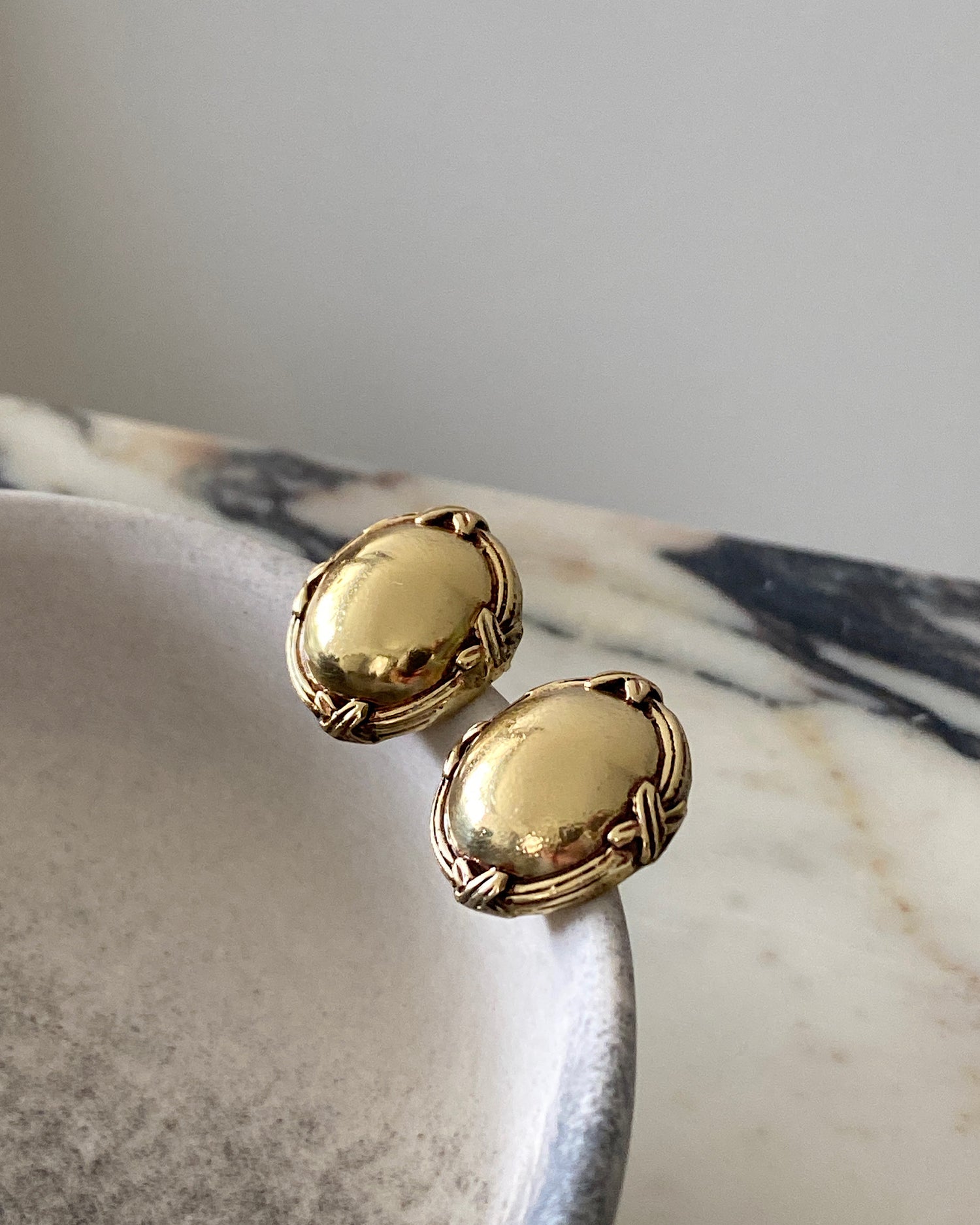 gold round flat earrings with an edge  details sit in a bowl